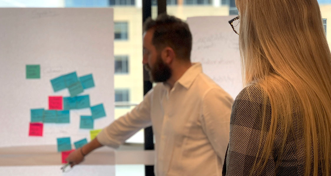 A photo of a group using sticky notes and wall-mounted flipchart paper to synthesise research results